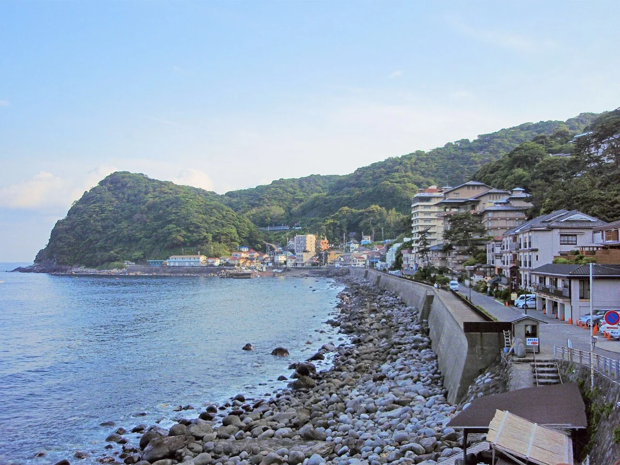Hokkawa hot-spring village along a rocky shore beneath green hills