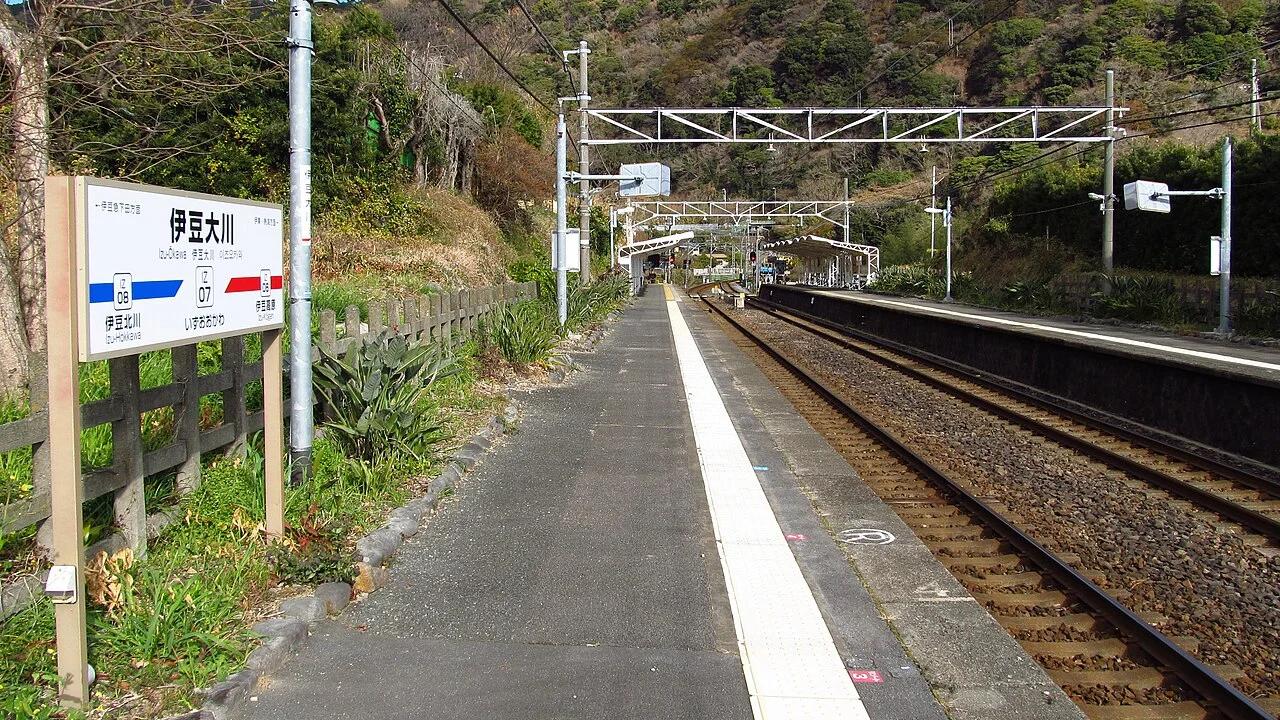 Izu-Okawa station platforms and railway tracks beside a wooded hillside