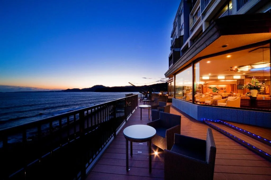 Seafront terrace and warmly lit hotel exterior at dusk at Inatori Tokai Hotel Yuen
